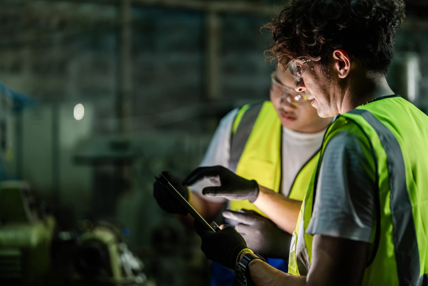 Dos trabajadores con gafas de protección consultan juntos una tableta en una planta industrial.